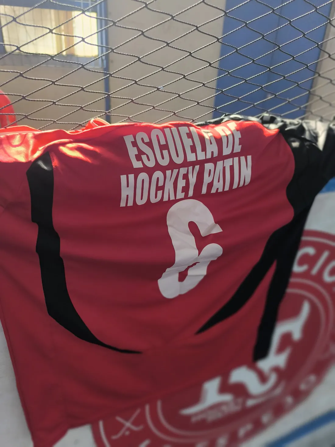 Camiseta de la Escuela de Hockey Patín colgada en la reja de la cancha
